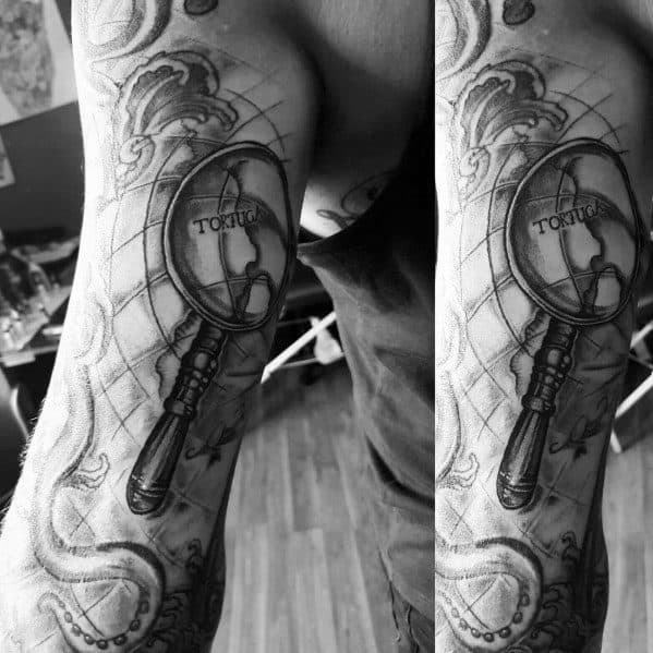 Tattoo featuring a magnifying glass highlighting "Tortuga" on a nautical map, surrounded by waves and intricate shading for a bold design.