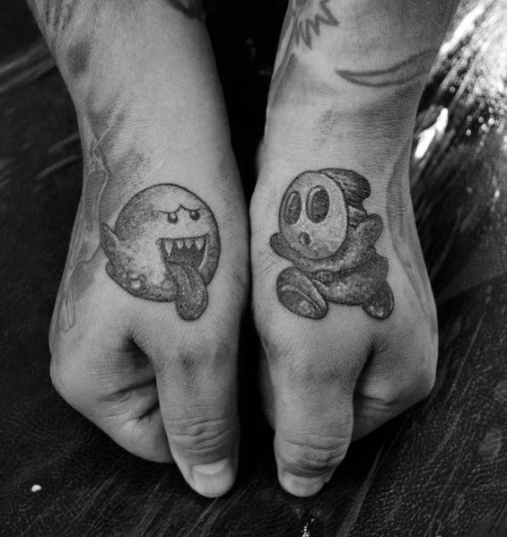 Matching Mario-themed hand tattoos featuring Boo with its tongue out on one hand and Shy Guy on the other, shaded in black and grey.