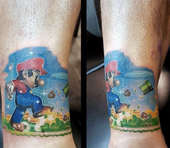 Colorful *Super Mario* wrap-around tattoo on the ankle, featuring a side-scrolling level with Mario, Goombas, pipes, and a classic pixel-art style.