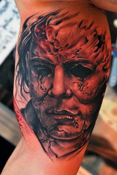 Intense Michael Myers tattoo with a burned, battle-worn mask, deep scars, and eerie shading for a terrifying horror effect.
