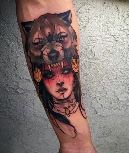 Neo-traditional tattoo of a woman wearing a fierce wolf headdress, detailed shading, bold colors, and tribal-inspired accessories.