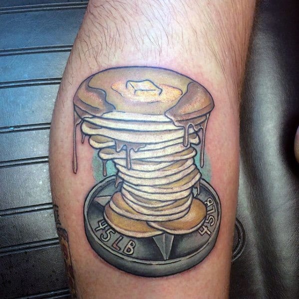Stack of pancakes tattoo melting over a 45LB weight plate, blending food and fitness with realistic shading and dripping syrup details.