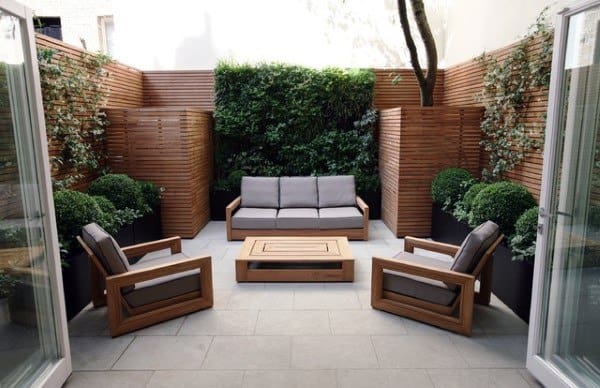 Cozy, modern patio with wooden furniture, gray cushions, and lush green plants