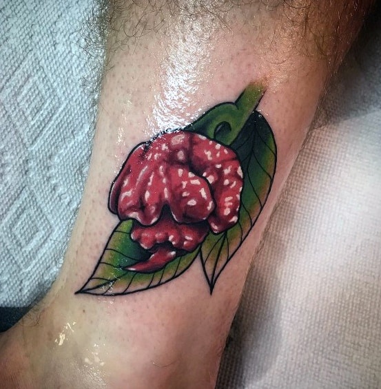 Realistic red chili pepper tattoo with a wrinkled texture, paired with a green leaf, creating a bold and vibrant design on the ankle.