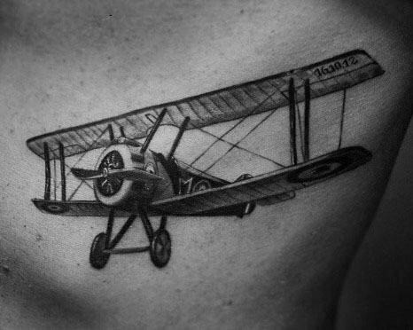 Black and grey chest tattoo of a vintage biplane with a detailed propeller, realistic shading, and fine linework for a classic aviation look.