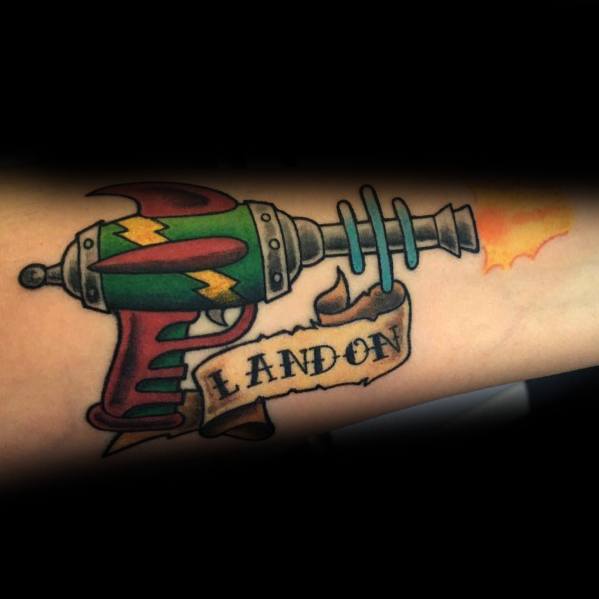Classic ray gun tattoo with a retro sci-fi design, featuring bold colors, lightning bolt details, and a banner with the name "Landon."