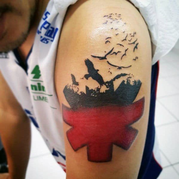 Upper arm tattoo featuring the Red Hot Chili Peppers logo blended with a silhouette of a jumping figure, birds, and a dynamic landscape.