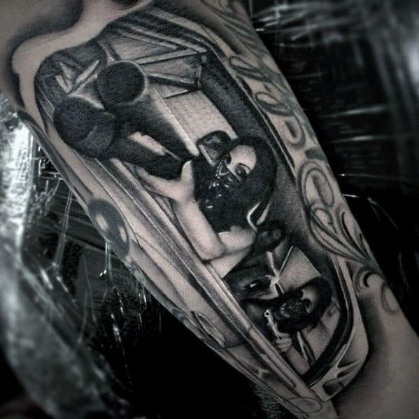 Black and grey tattoo of a masked figure aiming a shotgun from a car window, featuring intense shading and a dramatic, high-contrast design.