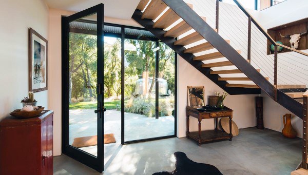 Spacious entryway with a wooden staircase, large glass door, and an outdoor view of greenery