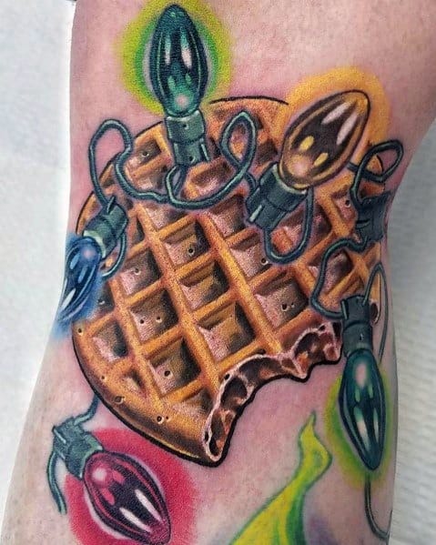Festive waffle tattoo with a bitten edge, wrapped in colorful glowing Christmas lights, blending holiday spirit with a love for breakfast.