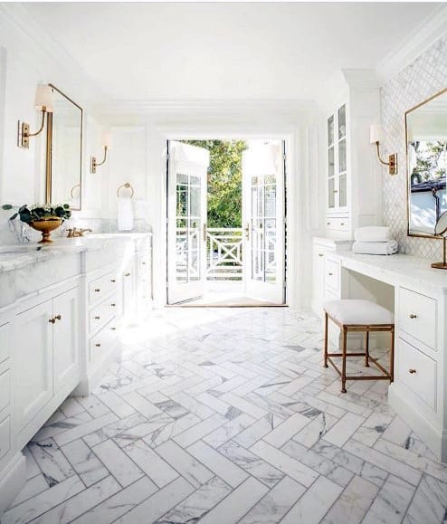 Bright white bathroom with marble flooring, gold accents, and French doors opening to a balcony.