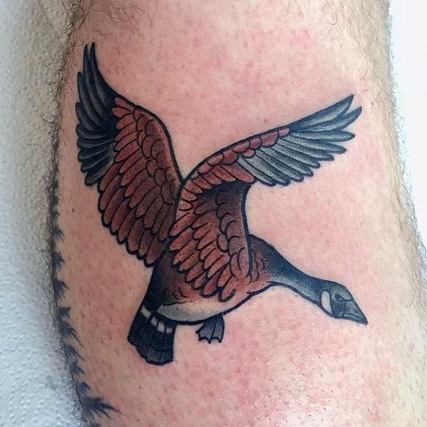 Traditional-style tattoo of a flying goose with bold black outlines and rich brown and gray shading, inked on the leg.