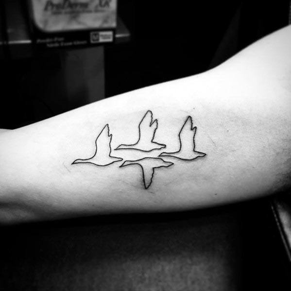 Minimalist black outline tattoo of four geese in flight, inked on the inner arm, creating a simple and elegant design.