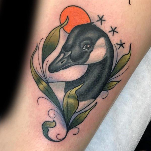 Traditional-style tattoo of a goose’s head framed by flowing leaves, with a red sun and three stars above, inked in bold colors and smooth shading.