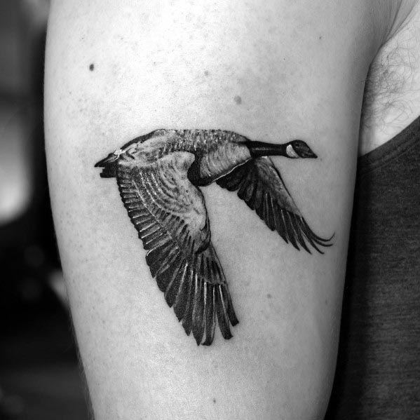 Realistic black and gray tattoo of a flying goose, inked on the upper arm with detailed feather shading and fine linework for a lifelike effect.