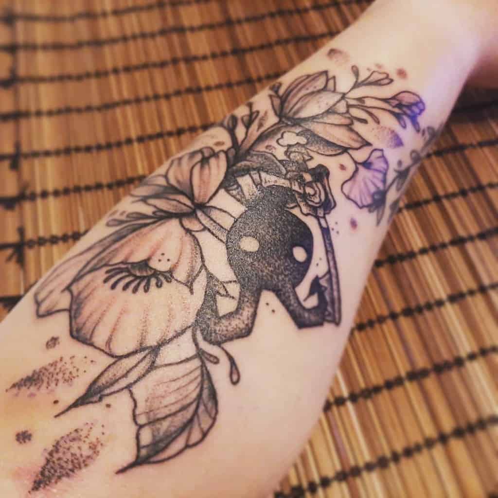 Kingdom Hearts tattoo of a Shadow Heartless holding a Keyblade, surrounded by detailed floral designs in black and grey ink on the forearm.