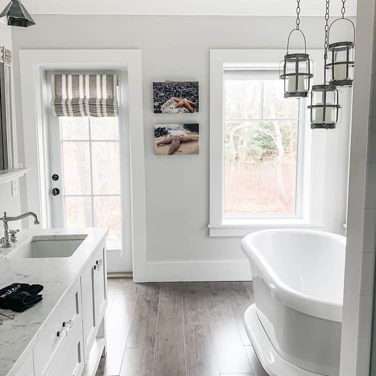 Farmhouse-style bathroom with a white tub, window, hanging lights, and a large mirror above a double sink vanity