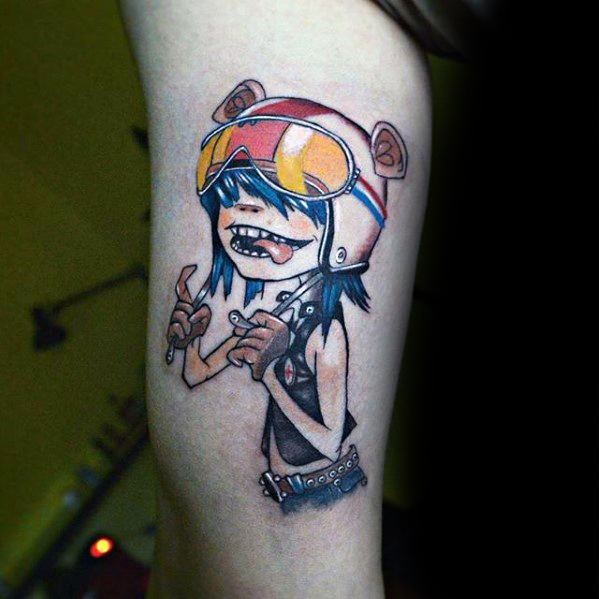 Color tattoo of Noodle from Gorillaz wearing a bear-eared helmet and goggles, grinning with hands raised in a playful pose.
