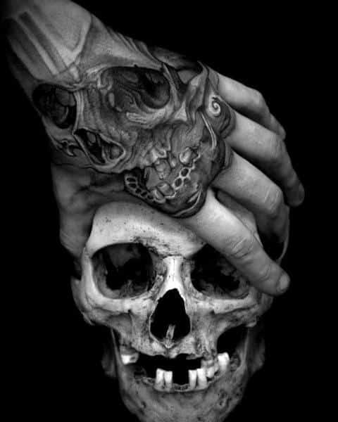 Black and grey tattooed hand gripping a realistic skull, featuring intricate skeletal designs on the fingers for a dark and gothic aesthetic.