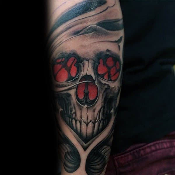 Bold gothic tattoo featuring a skull with red glowing eyes and intricate black and grey shading for a striking and eerie design.