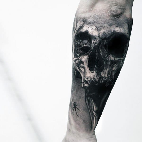 Black and grey forearm tattoo featuring a decayed skull with spiderwebs and a crawling spider for a dark and eerie gothic design.