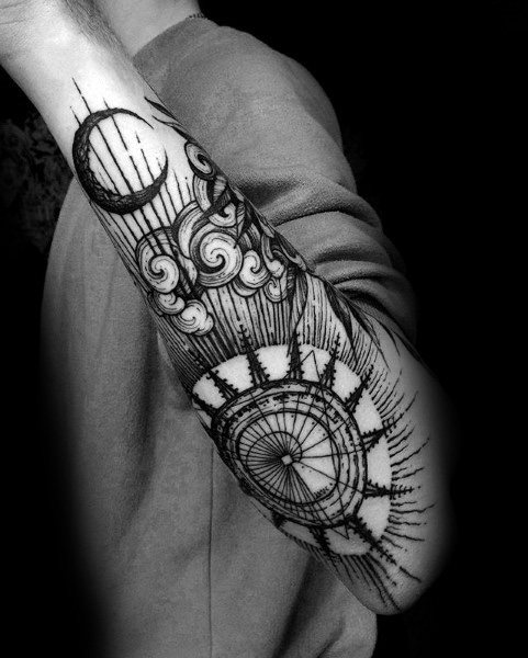 Black and grey forearm tattoo featuring a detailed compass, crescent moon, and swirling clouds, blending celestial and navigational elements in a gothic style.