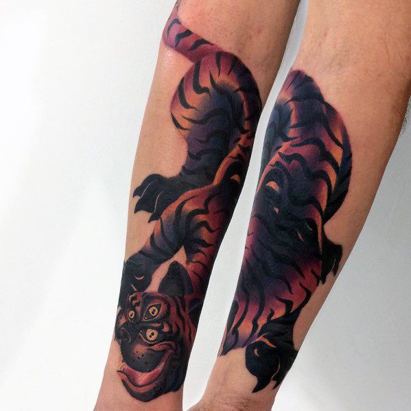 Bold gradient tiger tattoo in deep black, red, and orange tones, featuring a fierce expression and dynamic pose across both forearms.