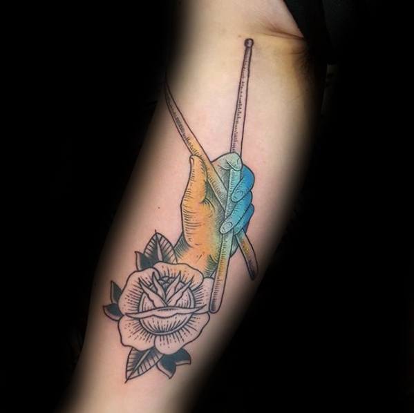 Tattoo of a hand holding drumsticks with a blue-to-orange gradient, paired with a black-outlined rose at the wrist.