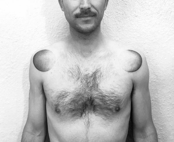 Symmetrical black and grey gradient tattoos on both shoulders, resembling shaded half-spheres or eclipses.