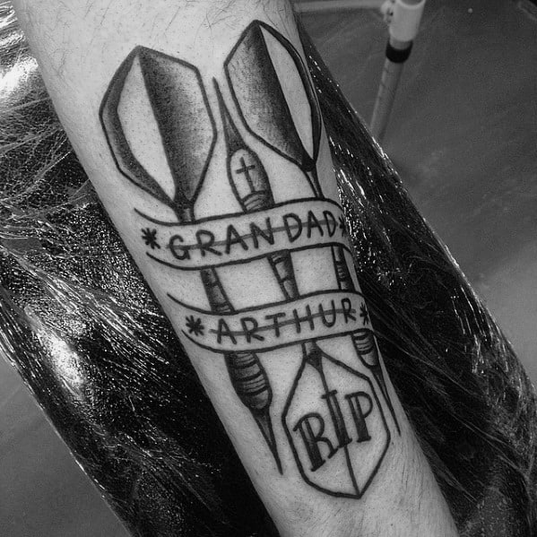 Memorial dart tattoo with three darts wrapped in banners reading “Grandad Arthur” and “RIP,” symbolizing tribute and remembrance.