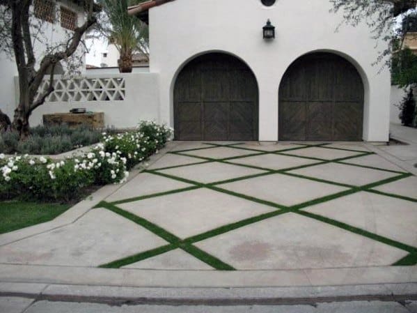 Elegant driveway with a crisscross concrete and grass pattern leading to double arched wooden garage doors.