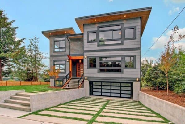 Modern two-story home with a driveway featuring grass and concrete slabs and a glass garage door.