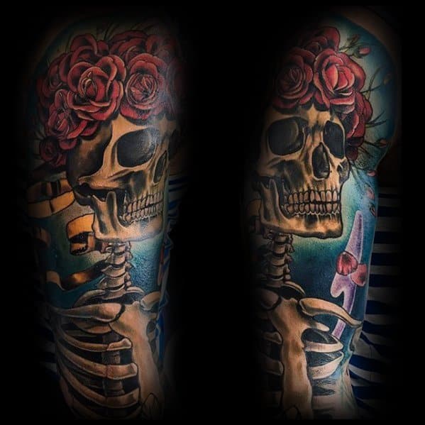 Grateful Dead skeleton tattoo with a crown of red roses, set against a blue sky background with purple flowers and golden ribbon.