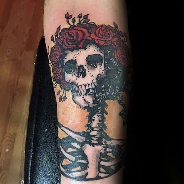 Grateful Dead skeleton tattoo with a crown of deep red roses, set against a soft orange background and bold black ribcage design.