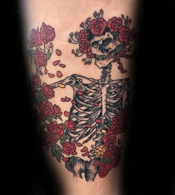 Grateful Dead skeleton tattoo surrounded by blooming red and yellow roses, with falling petals and a crown of flowers on the skull.