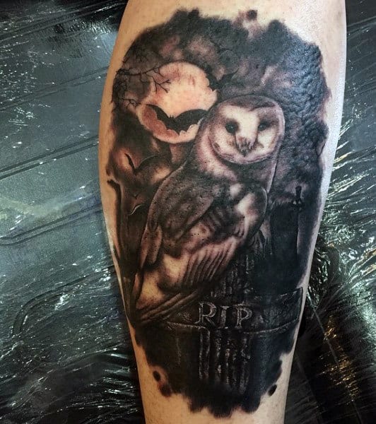 Tattoo of an owl perched on an "RIP" grave marker in a spooky graveyard, with a bat and full moon in the background