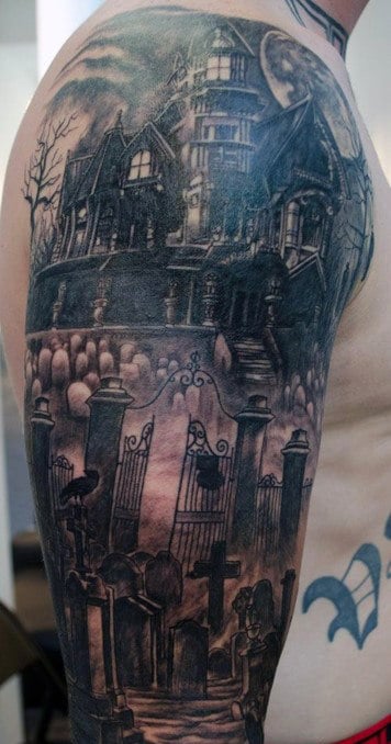 Tattoo of a haunted house on an arm with a graveyard and gothic gates in the foreground