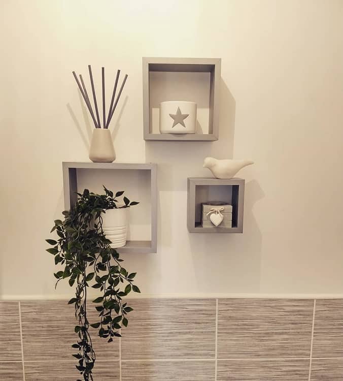 Bathroom with grey square floating shelves, potted plant, candle, and decorative accents.