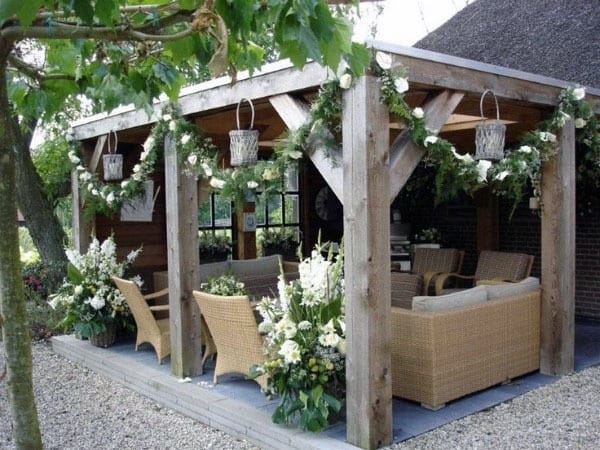 Rustic pergola with wooden beams, wicker furniture, floral garlands, and hanging lanterns.