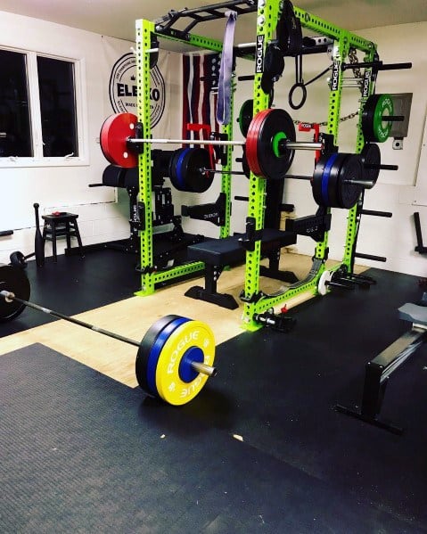 Garage gym with a vibrant green power rack, weight plates, lifting platform, and rubber flooring.