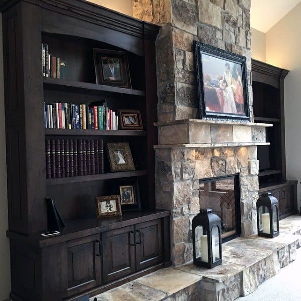 Rustic great room with dark wood built-in bookcases, stone fireplace, lanterns, and framed artwork