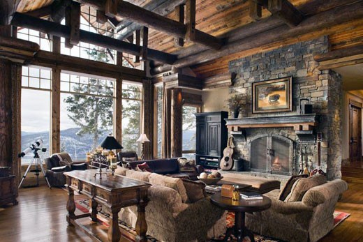 Spacious log cabin living room with stone fireplace, large windows, and cozy seating arrangement.