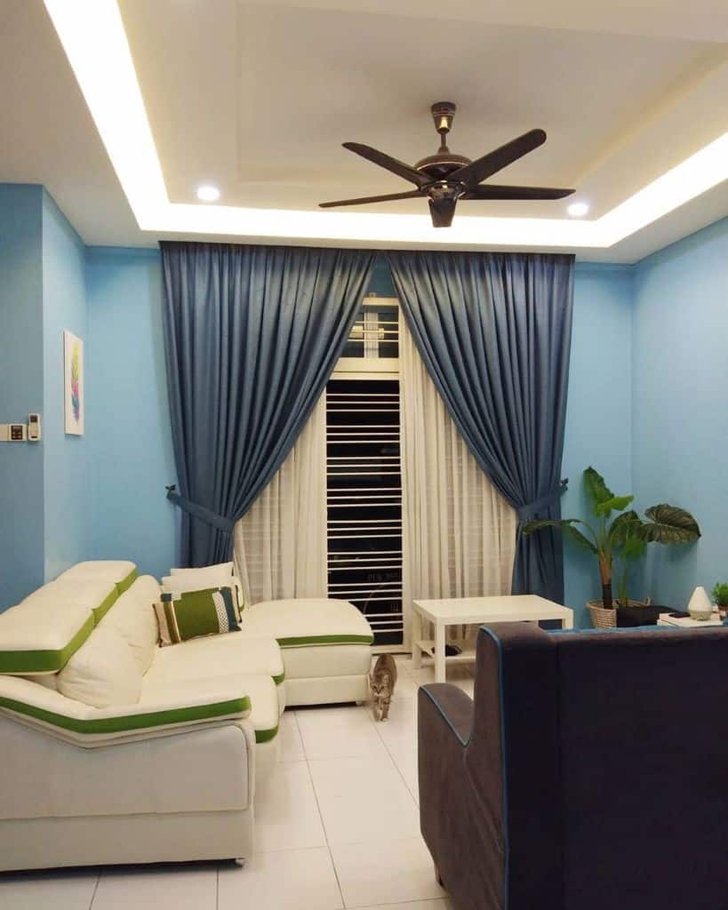 Bright living room with blue walls, white sectional sofa, green accents, and large curtains.