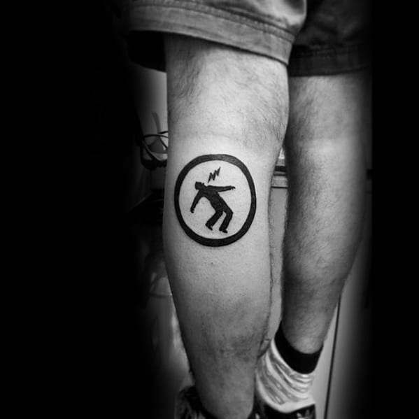 Tattoo of a black stick figure being electrocuted inside a circle, inspired by Green Day’s *Warning* album symbol.