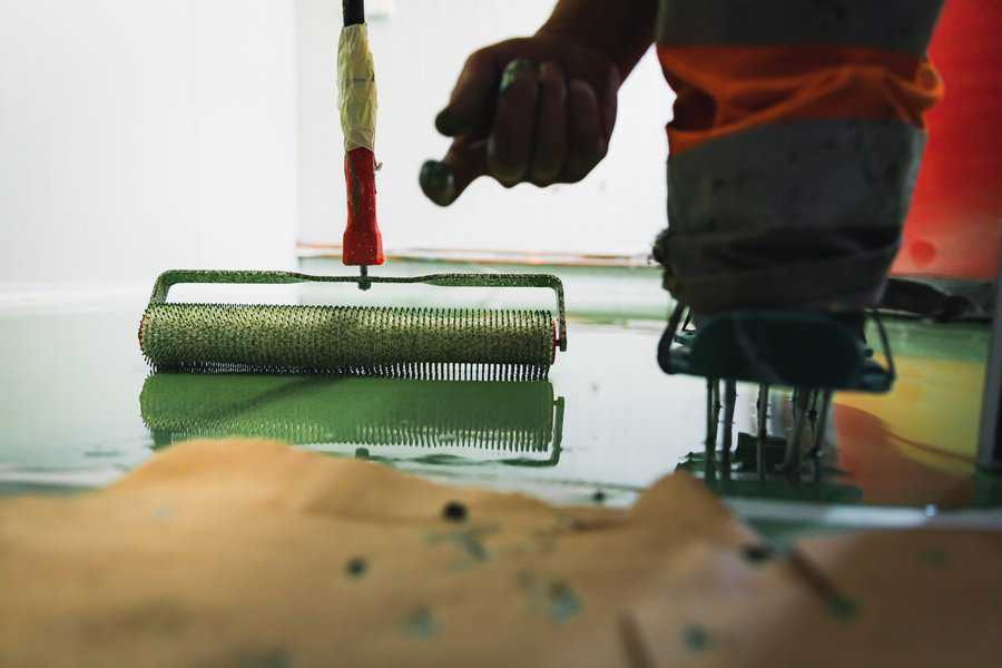 Worker applying green epoxy floor coating with a spiked roller tool.