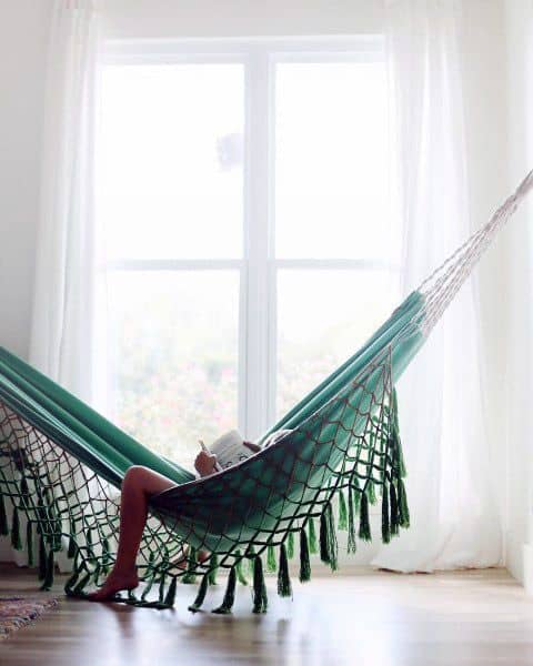 Green indoor hammock by a window with sheer curtains, perfect for relaxing and reading.