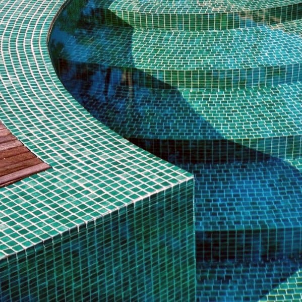 Curved pool design with vibrant green mosaic tiles and tiered steps for a modern look.