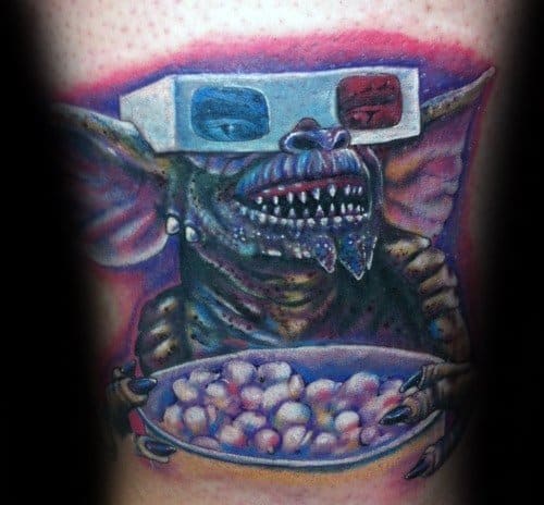 Realistic Gremlin tattoo with 3D glasses, sharp teeth, and a bowl of popcorn, capturing a fun movie-night vibe in vivid colors.