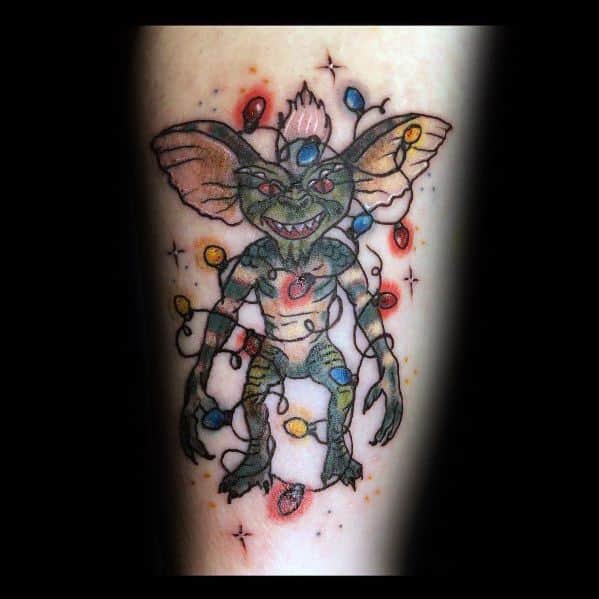 Gremlin tattoo wrapped in colorful Christmas lights, blending mischief with a festive holiday twist in a playful design.