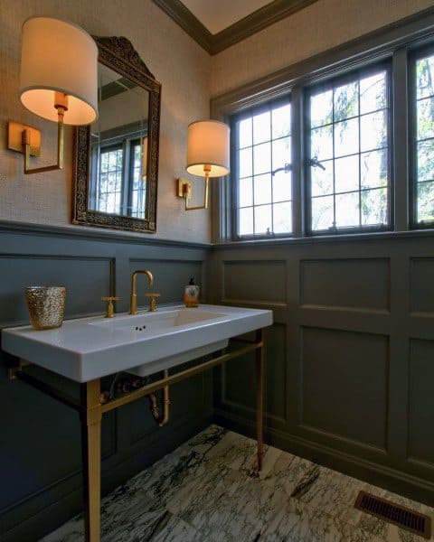 Bathroom with gray paneling, white vanity, gold fixtures, and wall sconces.